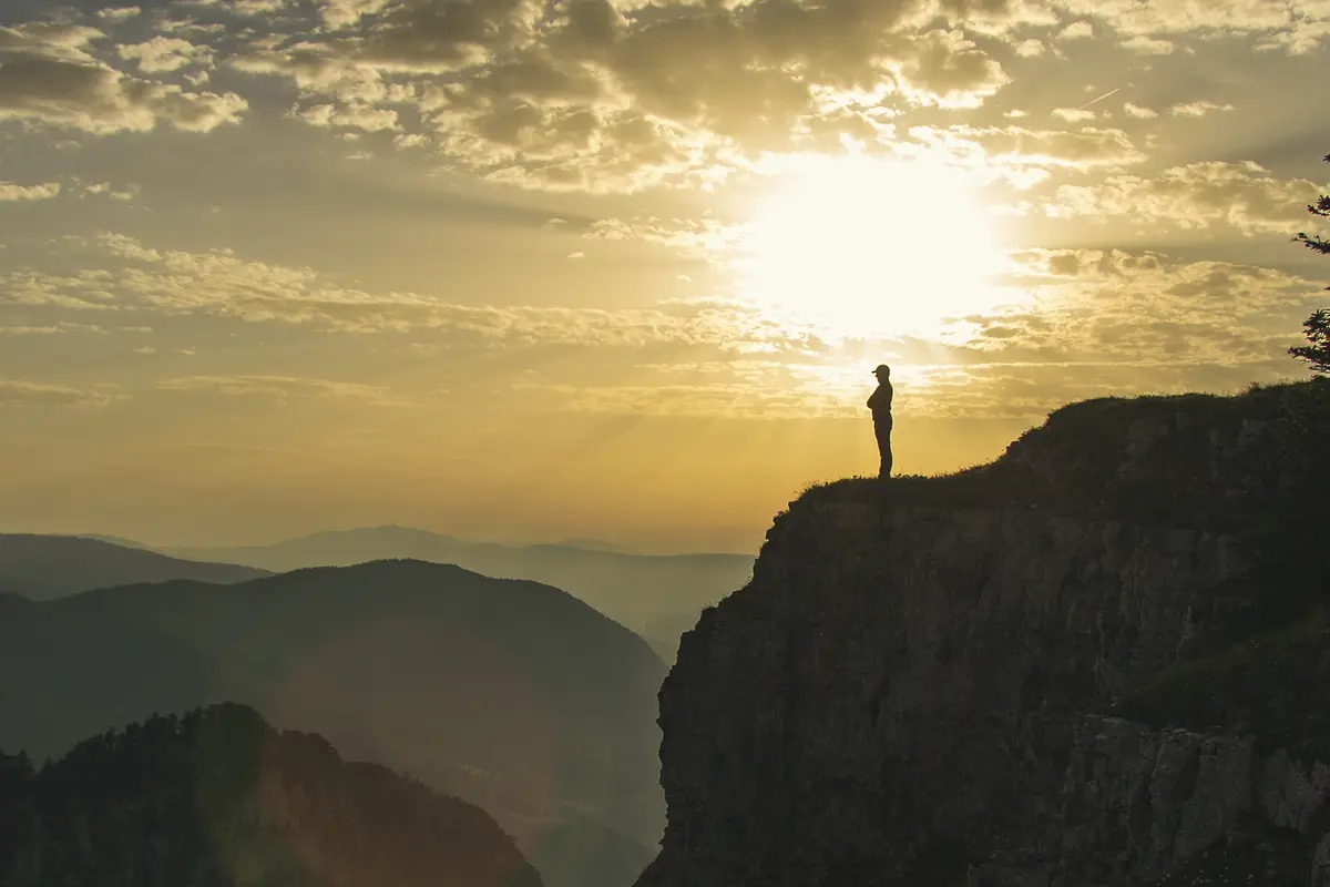 A hiker on the cliff edge of the Creux du Van at sunrise